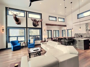 A spacious living area with a white leather sofa, blue armchairs, and a dining table. - Vista Azul Hideaway • Private Hot Tub • Mountain Views (Breckenridge)