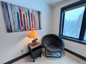 A room with a window, a lamp, a chair, and a wall art piece.