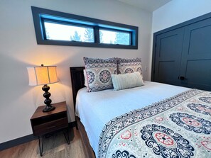 A bedroom with a bed, a nightstand, a lamp, a window, and a door. - Vista Azul Hideaway • Private Hot Tub • Mountain Views (Breckenridge)