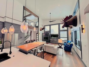 A modern kitchen with a central island, pendant lighting, and a dining area with a sofa and chairs.