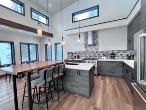 Una cocina moderna con una isla central, taburetes de bar y un ventanal grande.