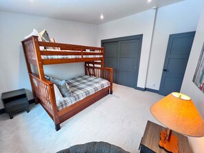 A bunk bed with a plaid mattress, a small bedside table, and a lamp on a wooden nightstand.