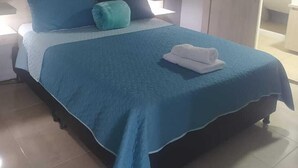 A neatly made bed with a blue bedspread and pillows, a bedside table with a lamp, and a view of a bathroom through an open door. - Hotel Mont Blanc (Circasia)