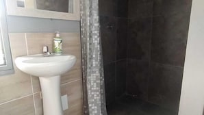 A bathroom with a pedestal sink, a mirror, a shower with a glass door, and a patterned shower curtain. - Hotel Mont Blanc (Circasia)
