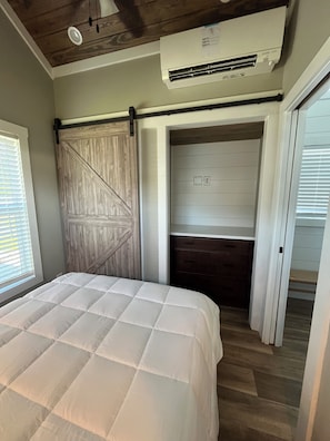 A bedroom with a bed, a wooden wardrobe, a built-in bench, and an air conditioning unit. - Circle T Mini Farms (Strawberry Plains)