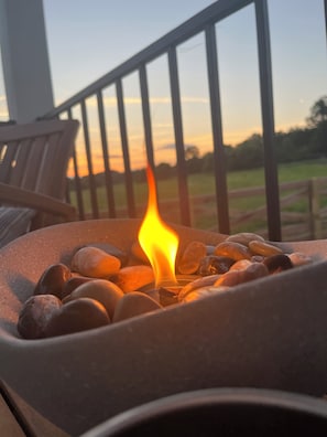 A fire pit with rocks and a flame, set on a balcony with a railing and a chair. - Circle T Mini Farms (Strawberry Plains)
