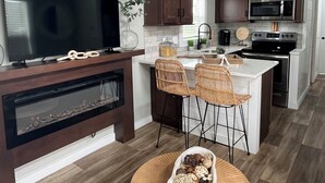 Una cucina moderna con mobili in legno scuro, un ampio televisore a schermo piatto, un forno integrato e un'area pranzo con sedie in vimini.