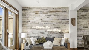 A living room with a rustic wooden wall, a grey sofa, and a coffee table with a vase. - Luxury 3BDRM - Chic Mountain Escape - BBQ/Fire Table (Canmore)
