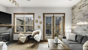 A modern living room with a fireplace, a large window, and a wooden accent wall. - Luxury 3BDRM - Chic Mountain Escape - BBQ/Fire Table (Canmore)
