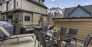 Une terrasse dotée d’une table à plateau en verre, de chaises en osier et d’un foyer extérieur.