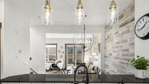 A modern kitchen with a black countertop, pendant lights, and a clock on the wall. - Luxury 3BDRM - Chic Mountain Escape - BBQ/Fire Table (Canmore)