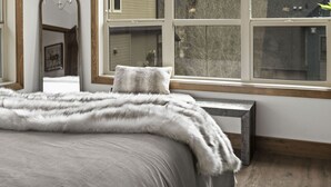 A bedroom with a large window, a chandelier, and a bed with a fur throw. - Luxury 3BDRM - Chic Mountain Escape - BBQ/Fire Table (Canmore)
