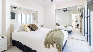 A bedroom with a bed, a bedside table, a mirror, a ceiling fan, and a sliding glass door leading to another room. - The Midas Touch | Rooftop Pool & Free Parking (Darwin City)