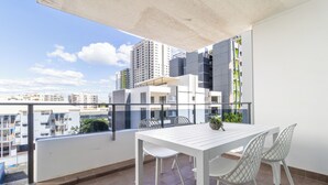 A balcony with a white table and chairs, a potted plant, and a view of surrounding buildings. - The Midas Touch | Rooftop Pool & Free Parking (Darwin City)