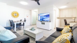 A modern living room with a flat-screen TV, a ceiling fan, a dining area, and a kitchen. - The Midas Touch | Rooftop Pool & Free Parking (Darwin City)