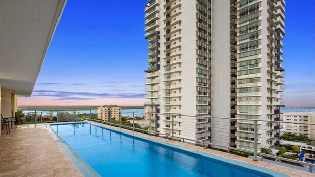 A modern high-rise building with a swimming pool on the ground floor. - The Midas Touch | Rooftop Pool & Free Parking (Darwin City)