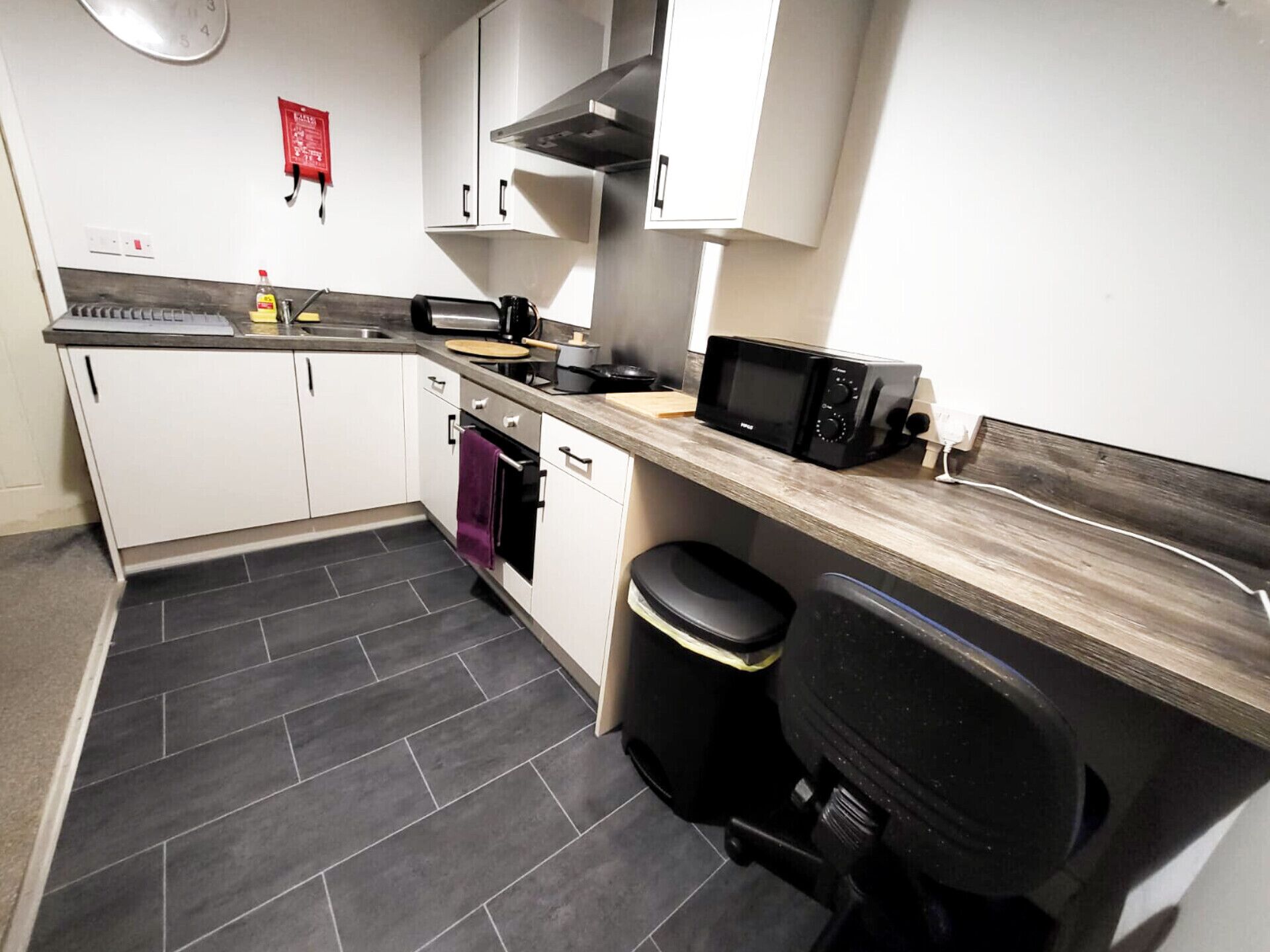 A compact kitchen with white cabinets, a microwave, a kettle, and a sink.