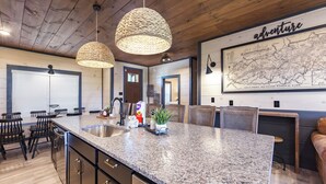 Une cuisine dotée de plans de travail en granit, d’armoires noires et d’un grand îlot central. On y trouve deux luminaires suspendus et une carte accrochée au mur.
