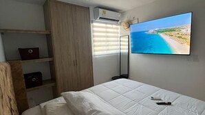 A bedroom with a bed, a wardrobe, a TV, and a window with blinds.