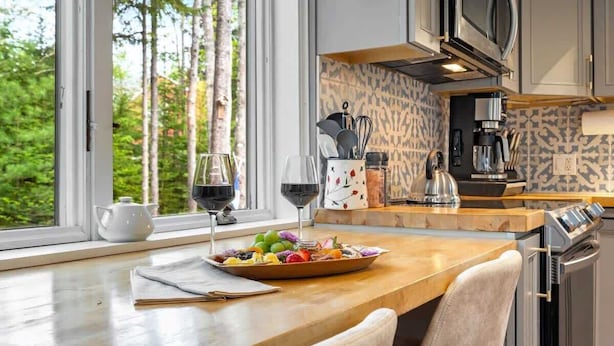 Una cocina moderna con encimera de madera, un bol de fruta, dos copas de vino y una cafetera.