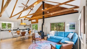 Un salón amplio con un sofá azul, techo de madera y un ventanal grande.