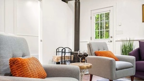 Una sala de estar moderna con dos sillones grises, una mesita de madera con copas de vino y un ventanal con vistas a la vegetación.