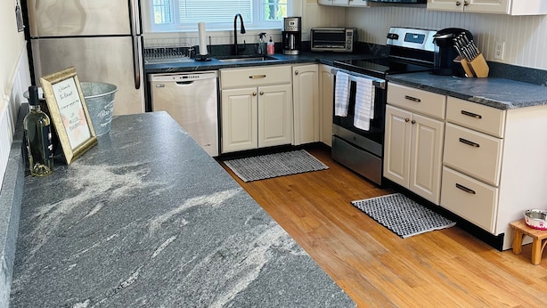Una cocina con armarios blancos, encimera de granito, refrigerador de acero inoxidable, microondas y estufa.