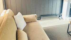 Una sala de estar moderna con un sofá color beige, un espejo redondo y un televisor de pantalla plana montado en la pared.