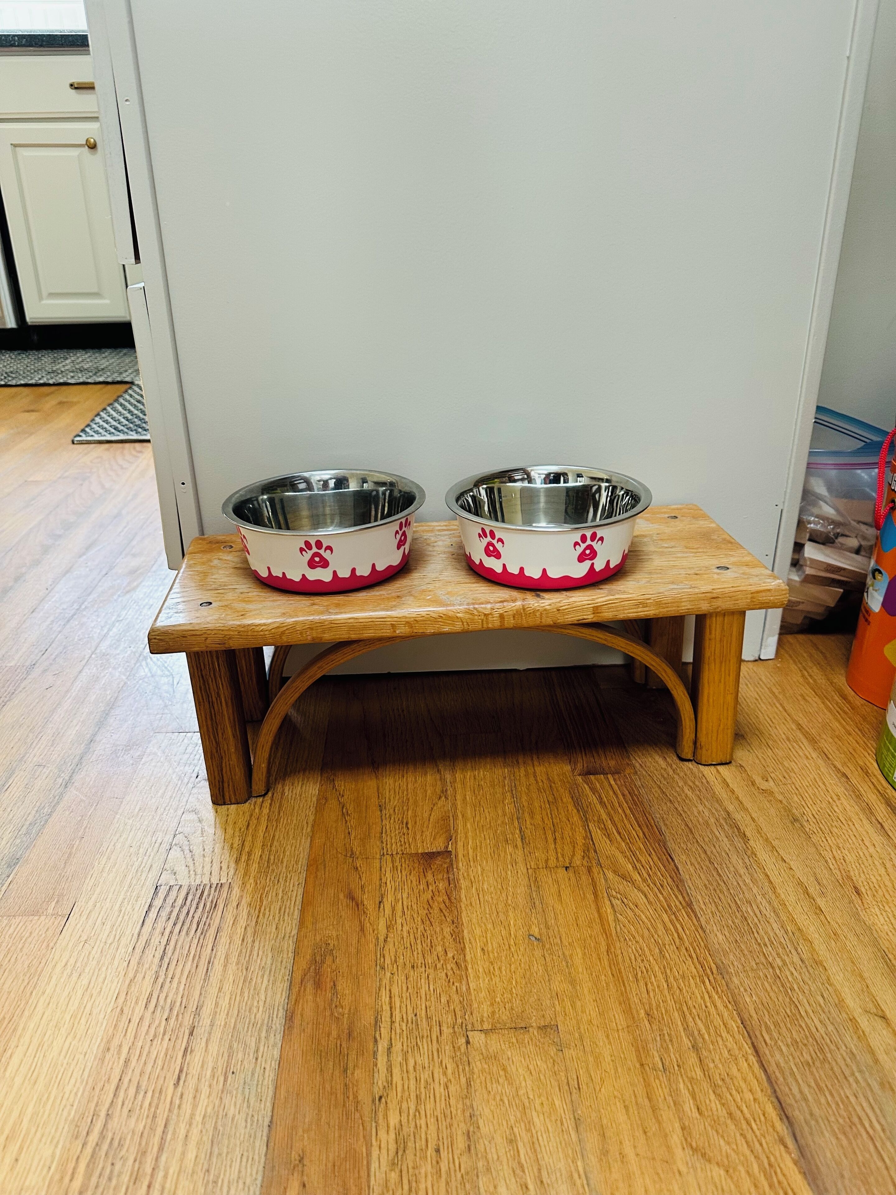 A wooden bench with two metal dog bowls on it.