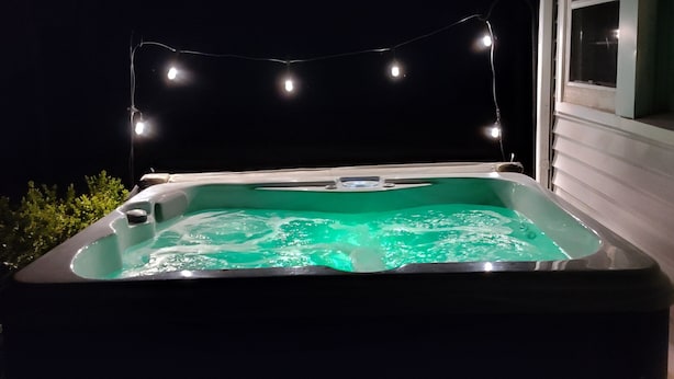 Un jacuzzi con una guirnalda de luces sobre él, frente a un cielo nocturno oscuro.
