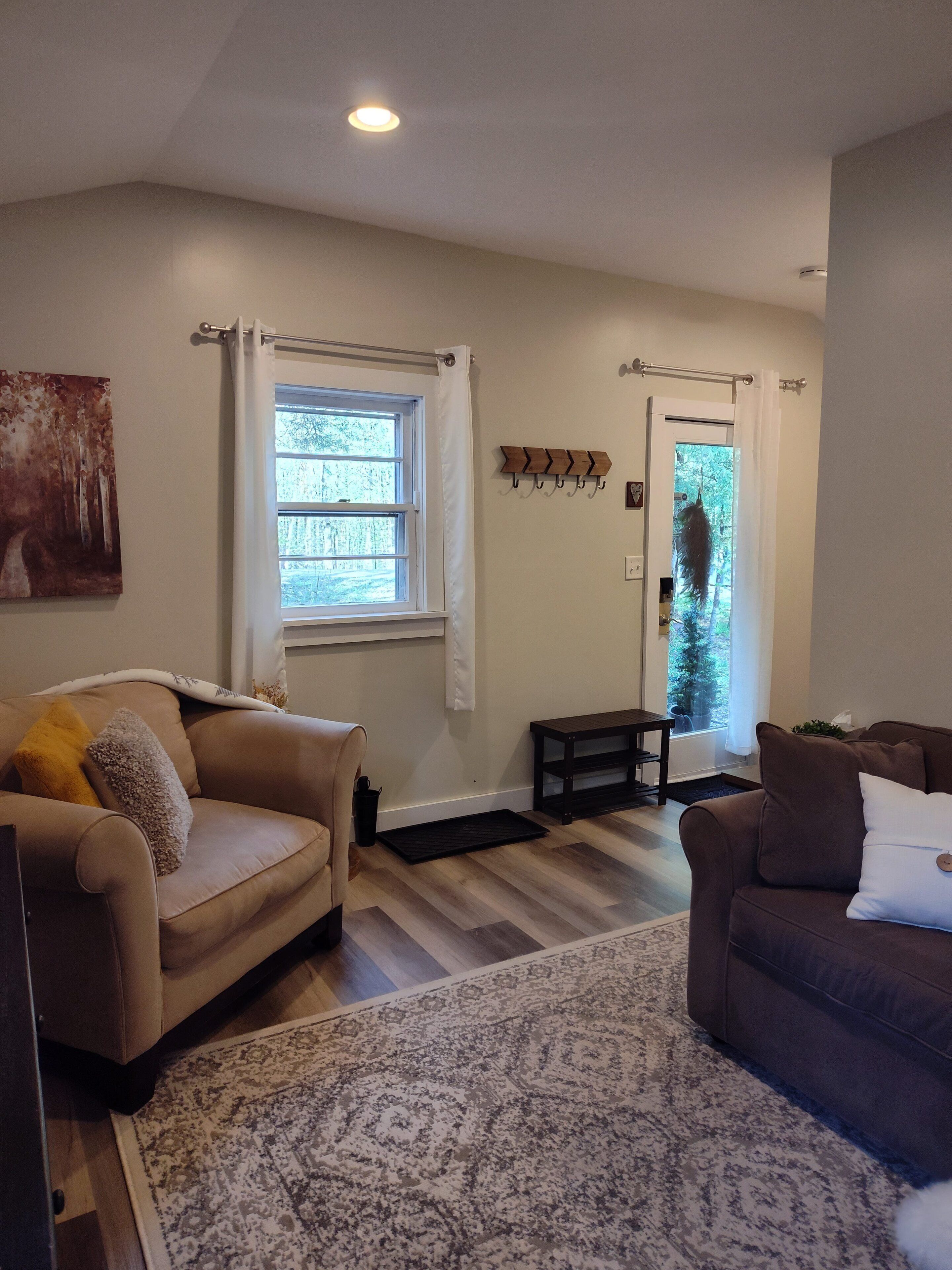 A living room with two sofas, a rug, a window with curtains, a coat rack, and a door leading outside.