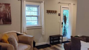 A living room with two sofas, a rug, a window with curtains, a coat rack, and a door leading outside.