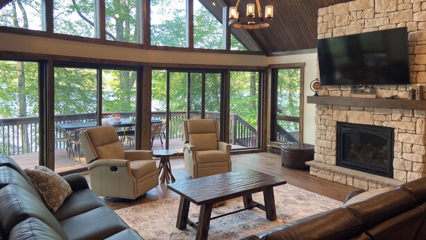 A spacious living room with a stone fireplace, leather sofas, and a large TV. - Lakefront Retreat with Private Dock and Hot Tub (Lackawaxen)