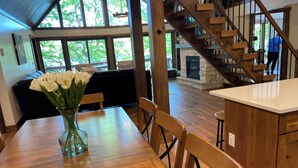 A wooden dining table with chairs and a vase of white flowers. A staircase leads to a stone fireplace. - Lakefront Retreat with Private Dock and Hot Tub (Lackawaxen)
