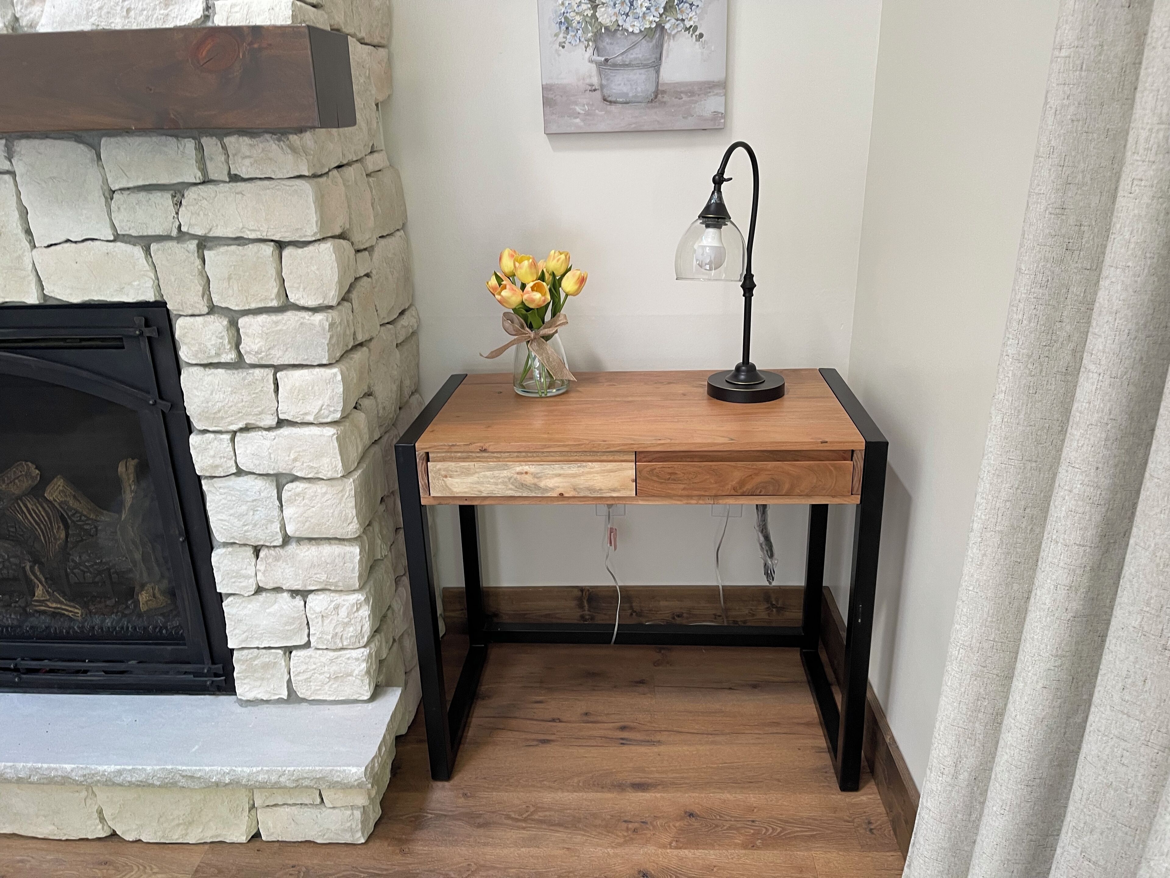 Un escritorio de madera con un florero, una lámpara y una chimenea con una pared de piedra.