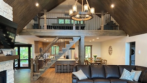 A spacious living area with a fireplace, a large leather sofa, a wooden coffee table, and a staircase leading to an upper level. - Lakefront Retreat with Private Dock and Hot Tub (Lackawaxen)