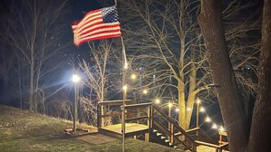 A nighttime outdoor scene with a flagpole, wooden stairs, and string lights. - Lake Life is for Everyone  (Maple Lake)
