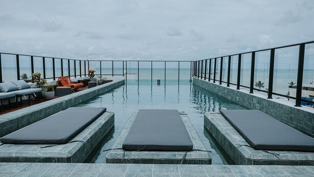 Piscina infinita no terraço, com cadeiras de lounge e guarda-corpo de vidro.