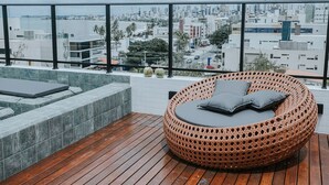 Terraço no telhado com uma poltrona de vime, um pequeno sofá e uma banheira de hidromassagem.
