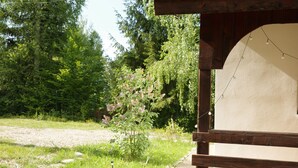 Una estructura de madera con pared blanca y luces colgantes, rodeada de follaje y árboles.