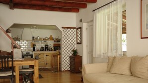 Una sala de estar acogedora con una mesa y sillas de madera, un sofá color beige y una cocina al fondo.