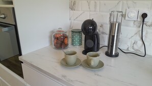 Un comptoir de cuisine avec une machine à café, un bocal en verre rempli de sachets de thé et deux tasses posées sur un pare-feu en marbre.