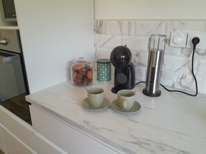 A kitchen counter with a coffee maker, a glass jar of tea bags, and two cups on a marble backsplash.