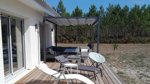 Une terrasse en bois avec des meubles d’extérieur, une pergola et une vue sur une forêt.