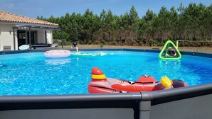 Une piscine avec des jeux gonflables, un patio couvert et un paysage boisé en arrière-plan.