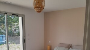 Une chambre dotée d’un grand lit, d’une table de chevet avec une lampe et d’une porte-fenêtre coulissante donnant sur un espace extérieur.