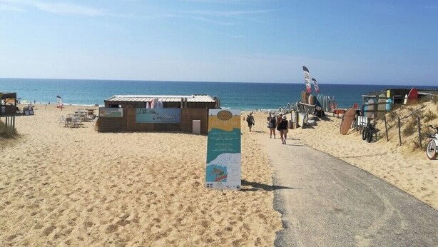 Une plage avec un panneau indicateur, un sentier sablonneux et des chaises de plage.