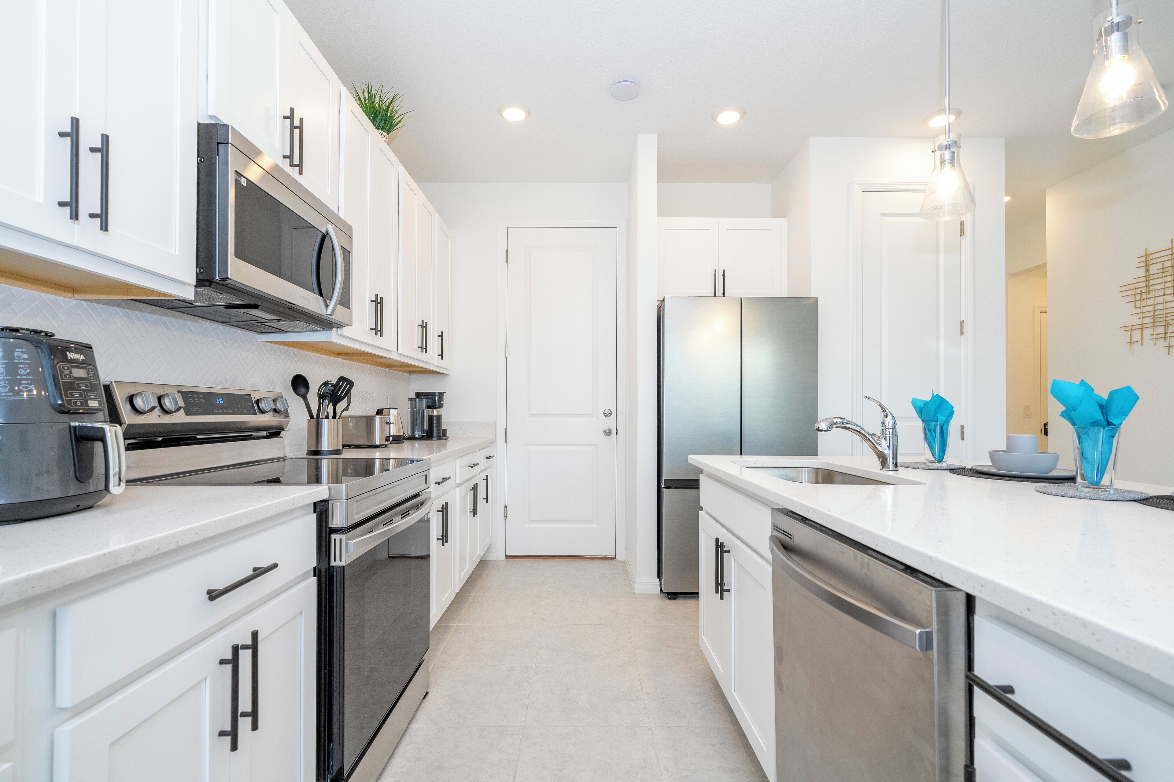 A modern kitchen with stainless steel appliances, white cabinetry, and pendant lighting.