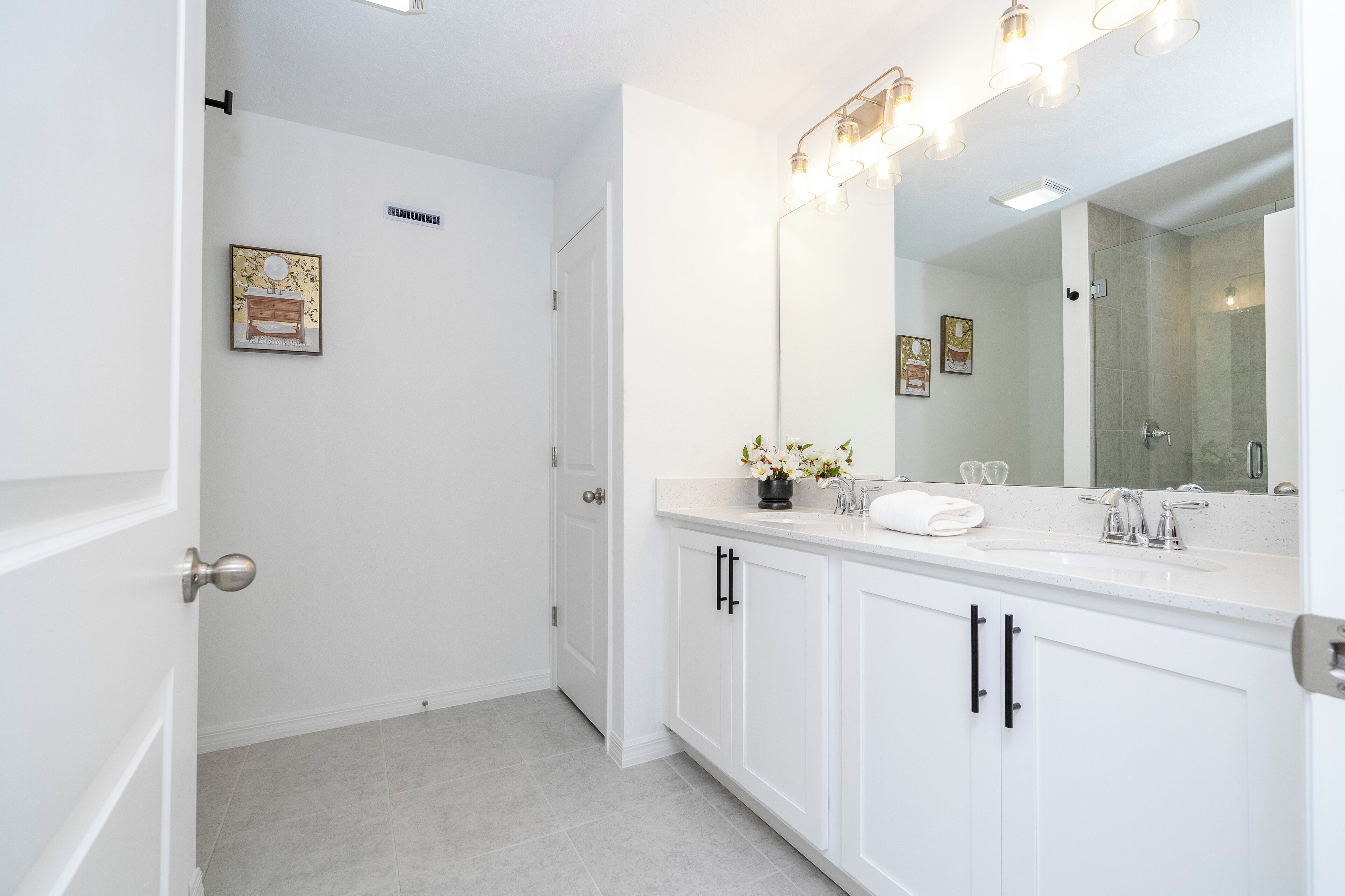A modern bathroom with white cabinetry, a large mirror, and a shower area.