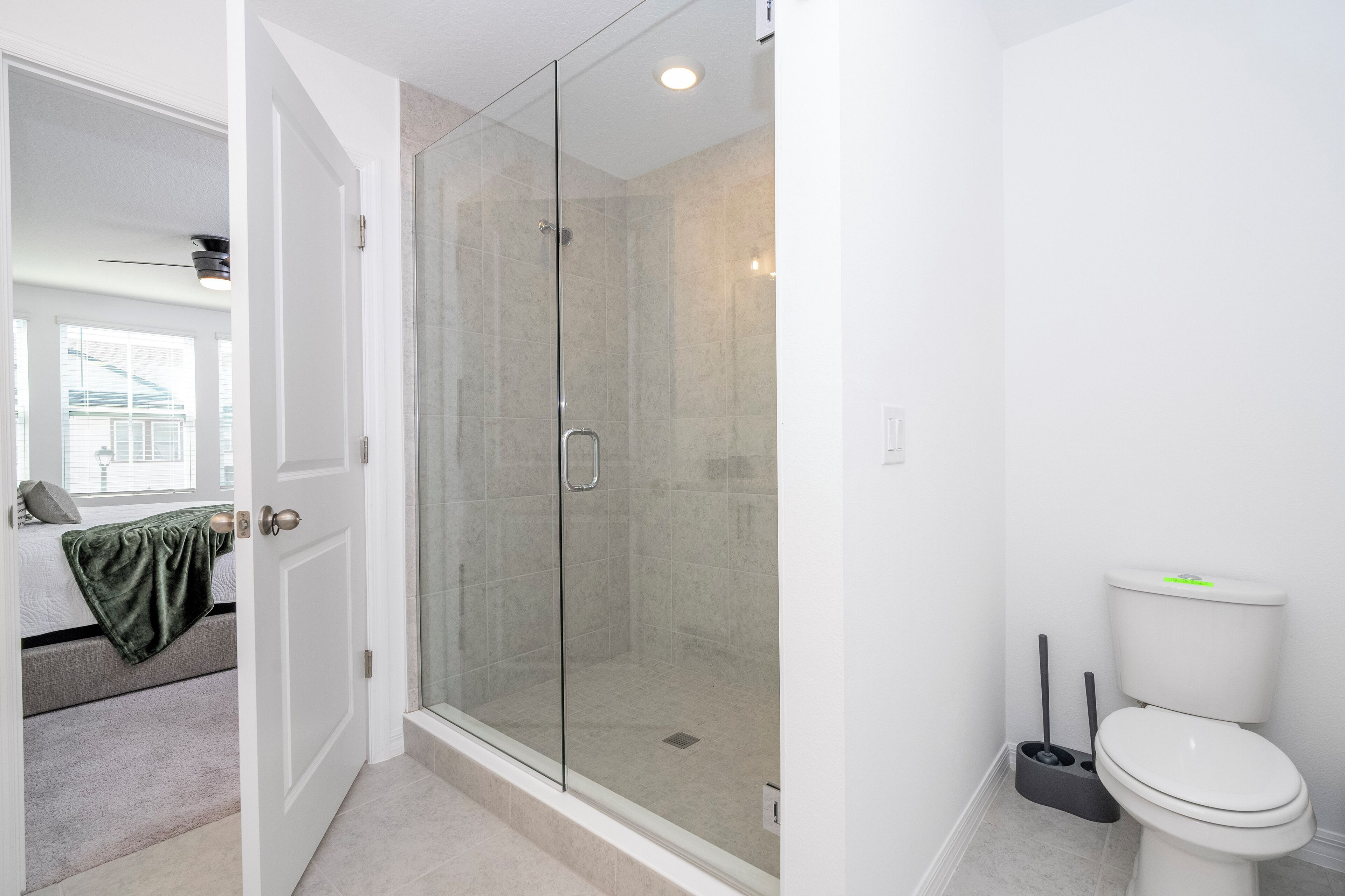 A modern bathroom with a glass-enclosed shower, a toilet, and a visible window in the adjacent room.